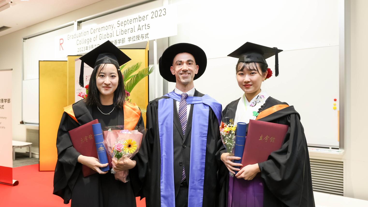 Three people standing in graduation robes and hats